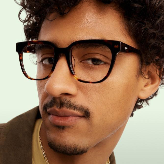 Man wearing glasses and a brown jacket with a neutral background